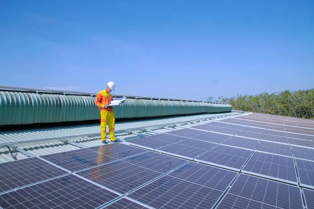 Engineer reviewing drawings while standing on a factory rooftop solar array